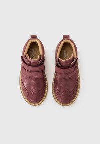 Burgundin väriset nilkkakengät kiiltävällä pinnalla, joissa on tarranauhat, brogue-koristeet ja vaaleanbeige kumipohja. Pehmeä sisävuori.