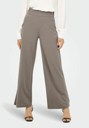 Grijze wijde broek van zachte stof, met een hoge taille en zijzakken, gecombineerd met een witte blouse en zwarte hoge hakken sandalen.