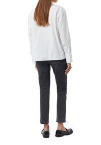 Biała długa koszula z luźnym krojem, zestawiona z ciemnoszarymi slim fit dżinsami i błyszczącymi czarnymi mokasynami, widziana z tyłu.