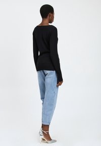 Schwarzer Pullover mit langen Ärmeln aus weichem Material, kombiniert mit hellblauen, umgeschlagenen Denim-Hosen und silbernen High Heels.