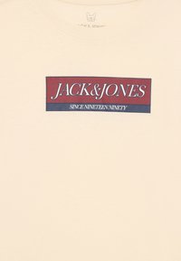 Kremfarget bomull T-skjorte med en mørkerød og blå rektangulær logo med teksten "JACK&JONES" og "SINCE NINETEEN NINETY".