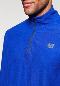 Blå, zip-up träningsoverdel med texturerad tyg, en mock collar och en liten grå logo på vänster bröst.