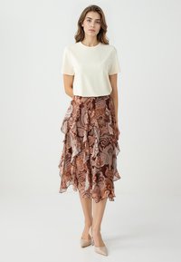 Crème top met korte mouwen gecombineerd met een vloeiende bruine rok met paisleypatroon, met gelaagde ruffles en een lichte textuur.
