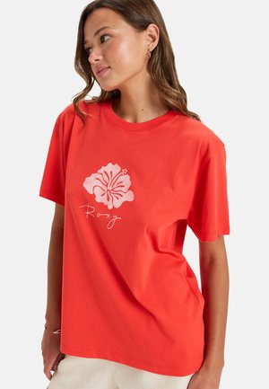T-shirt en coton rouge avec un graphique de fleur d'hibiscus blanche et le texte "Roxy". Coupe décontractée avec des manches courtes et un col rond.
