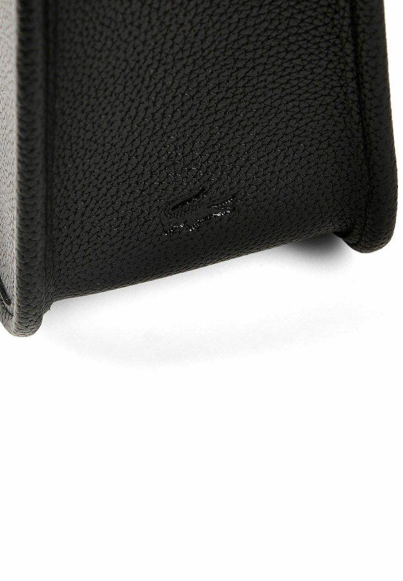 Coin d'un sac à main en cuir texturé noir avec logo crocodile embossé sur une surface lisse, sur fond blanc.