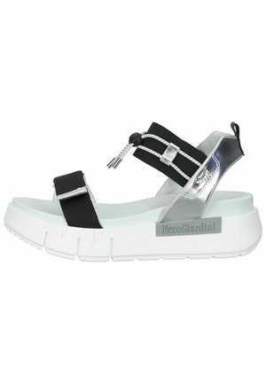 Black and silver platform sandals with elastic straps, metallic accents, and a white chunky sole featuring a textured design.