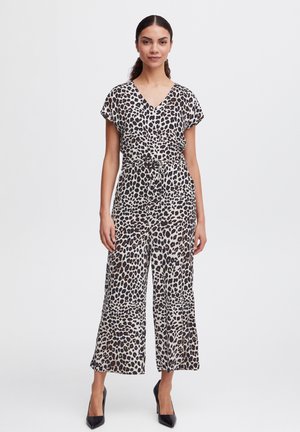 Jumpsuit s uzorkom leptira od mekog materijala, s V-izrezom, kratkim rukavima i pojasom u struku, u kombinaciji s crnim visokim potpeticama.