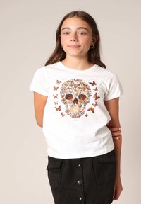 Witte T-shirt met een kleurrijk skeletontwerp gemaakt van vlinders, omringd door extra vlinderprints, met een ronde hals.