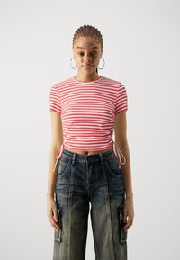 Rød og hvit stripete crop top med korte ermer, som har rynkede sider og knyting, parret med løstsittende, bleket blå denim cargo bukser.