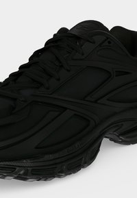 Baskets de sport noires avec un design complexe de panneaux, semelle épaisse texturée et fermeture à lacets, vues en angle latéral.