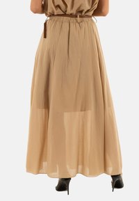 Falda maxi de color beige claro, hecha de un material fluido. Presenta una cintura elástica con un lazo y una capa transparente para añadir textura.