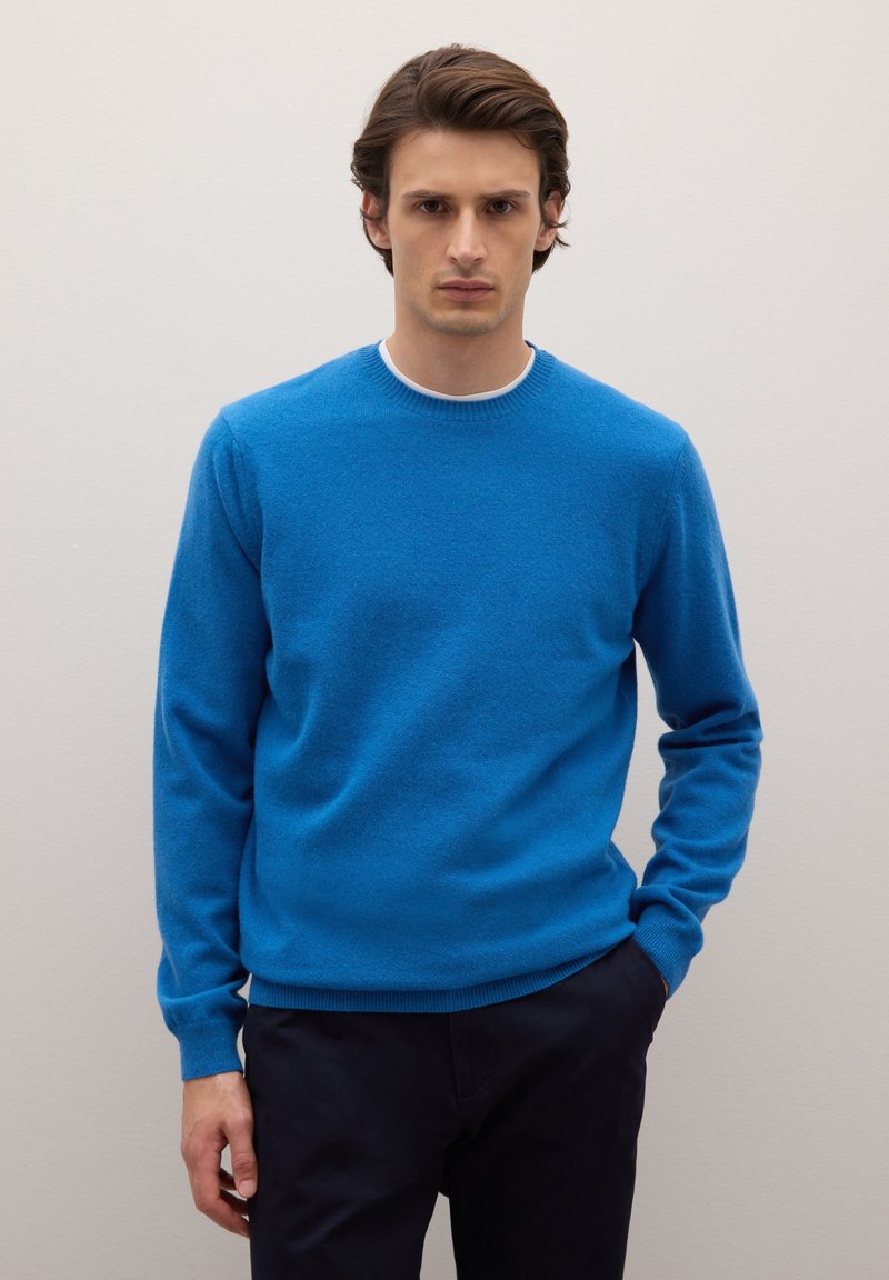 Blauer Pullover aus weichem Material mit Rundhalsausschnitt, langen Ärmeln sowie gerippten Bündchen und Saum. Trägt man über dunkler Hose.