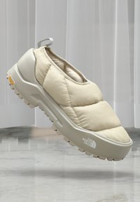 Chaussure à enfiler rembourrée beige avec une tige texturée, une semelle intermédiaire blanche épaisse et une semelle extérieure en caoutchouc robuste. Dispose d'une languette arrière et d'un détail de logo.