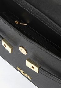 Interno di una borsa nera sintetica con una tasca con zip, accessori in tono oro e una texture liscia con un motivo sottile.