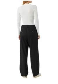 Biała bluzka z długim rękawem i raglanowymi rękawami, zestawiona z czarnymi, szerokimi spodniami z tylnymi kieszeniami i ozdobnymi guzikami.