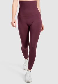 Høj talje, vinrøde leggings lavet af strækbart stof med en glat tekstur og tætsiddende pasform, parret med hvide træningssko.