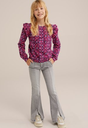Blusa rosa de manga larga con hombros rizados y un diseño estampado, combinada con jeans acampanados gris claro con aberturas en el dobladillo.