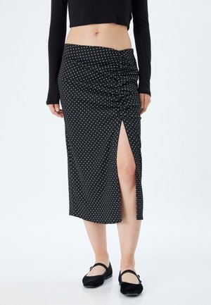 Zwarte midi-rok met polkadots, voorzien van een geraffineerd ontwerp, hoge split en zachte, gestructureerde stof. Gestyled met een zwarte lange mouwen top en platte schoenen.