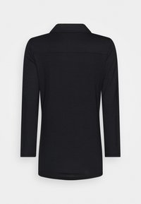 Chemise noire à manches longues avec col, fabriquée en tissu lisse. Présente une coupe droite avec un léger détail de couture dans le haut du dos.