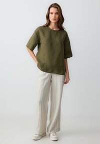 Olijfgroene linnen top met korte mouwen gecombineerd met lichtbeige gestreepte wijde broek en witte sneakers. Eenvoudig ontwerp, ontspannen pasvorm.