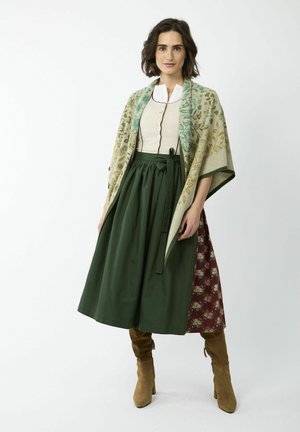 Traditionele outfit met een gebloemd sjaal, een crèmekleurige top met knopen en een groene rok. Bruine enkellaarsjes maken de look compleet.