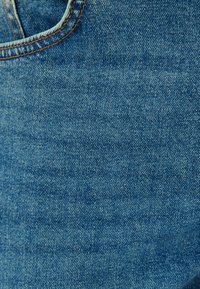 Tejido de mezclilla en un color azul medio con un tejido texturizado, que presenta costuras naranjas a lo largo de los bordes y un bolsillo inclinado.