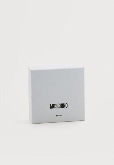 Boîte Moschino Milano blanche avec texte noir, posée sur une surface blanche devant un fond blanc uni.