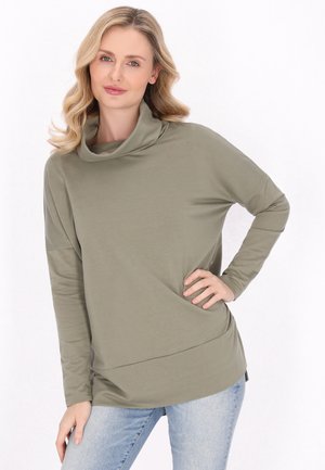 Lys grøn cowl-neck langærmet top lavet af blødt stof, med en løs pasform og asymmetrisk kant, parret med blå jeans.