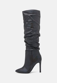 Botas pretas sintéticas até ao joelho com um design descaído, bico fino, e um alto salto agulha. Superfície texturizada com um brilho subtil.