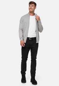 Sudadera de cremallera gris claro sobre una camiseta blanca, combinada con pantalones negros y botas. Tiene un corte relajado con puños y cuello acanalados.