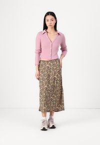 Světle růžový žebrovaný zkrácený cardigan s límečkem a knoflíky, spárovaný s dlouhou květinovou sukní s vícebarevným vzorem, nošený s lehkými teniskami.