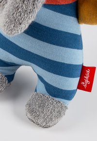 Giocattolo di peluche a strisce con piedi in tessuto grigio, etichetta rossa e orecchie grigie testurizzate. Strisce orizzontali blu e azzurre sul corpo.