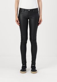 Crne skinny hlače od umjetne kože s glatkom teksturom, sa prednjim džepovima, kopčanjem na gumb i uskim krojem, uparene s crnim tenisicama.