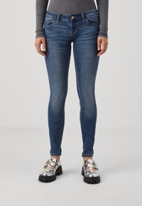 Jeans skinny azul con ligero desgastado, diseño de cinco bolsillos y cierre de botón. Combinados con zapatos plateados de suela gruesa.