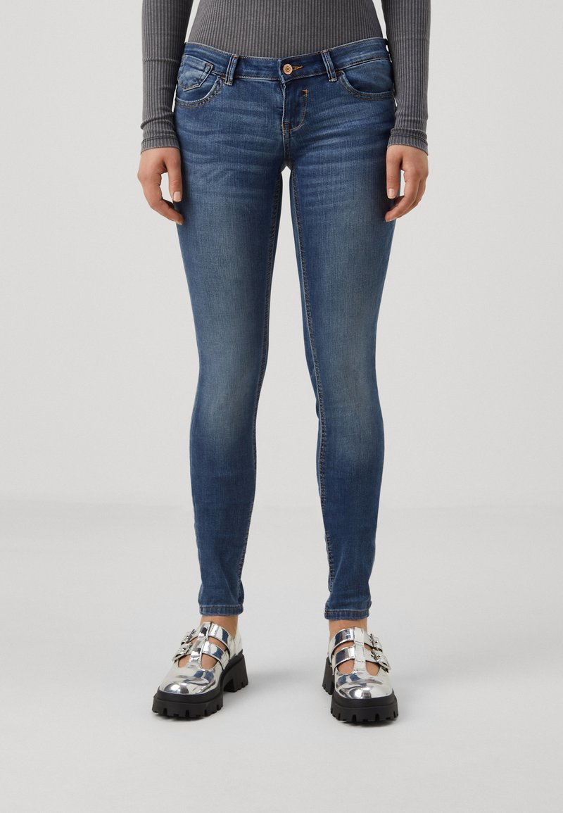 Jeans skinny azul con ligero desgastado, diseño de cinco bolsillos y cierre de botón. Combinados con zapatos plateados de suela gruesa.