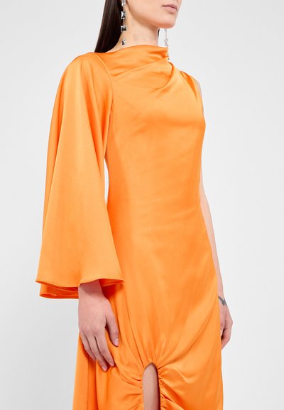 Oranssi mekko, jossa on laskostettu olkapää ja kellohihansuunnittelu. Keskipitkä, sivu on rypytetty ja siinä on halkiovyö. Silkkinen, teksturoitu kangas.