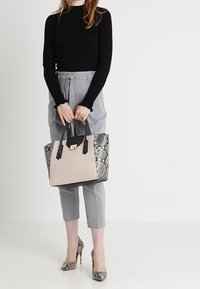 Beige tygväska med ormskinnsmönstrade sidor, svarta handtag och detaljer i guld. Modellen har på sig grå byxor och klackar med ormskinnsmönster.