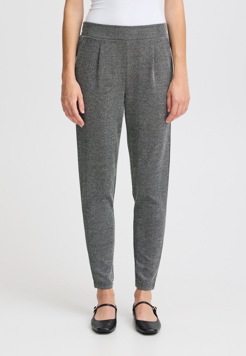 Grå herringbone-byxor med en åtsittande midja, svaga veck fram, och avsmalnande ben, tillsammans med svarta ballerinas.