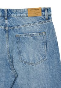 Jeans in denim blu chiaro con una tasca posteriore, cuciture gialle a contrasto e un'etichetta in pelle marrone al punto vita, caratterizzati da una texture sbiadita.