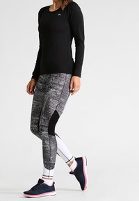 Schwarzes langärmliges Sportshirt, kombiniert mit strukturierten Leggings in Schwarz-Weiß-Muster. Tragen mit marineblauen Turnschuhen mit rosa Akzenten.