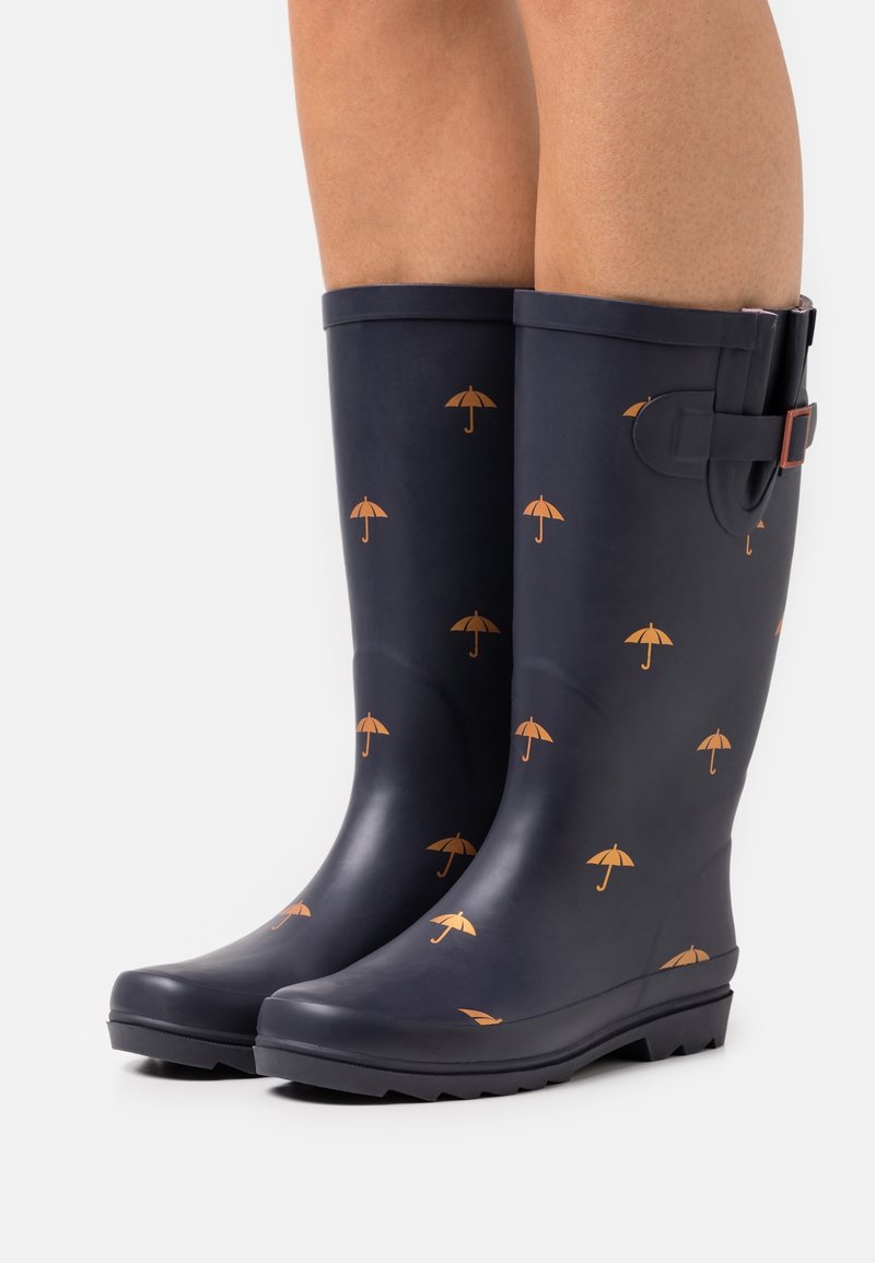 Bottes en caoutchouc navies avec une finition brillante, ornées d'un motif de petits parapluies orange et d'une boucle sur le côté.