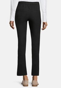 Schwarze Leggings mit einem taillierten Bund, zwei Gesäßtaschen und einem leichten Schlag am Saum; leichtes Material mit glatter Textur.