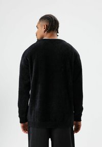 Zwarte, pluizige trui met een losse pasvorm, lange mouwen en een geribde zoom. Zachte textuur, eenvoudig ontwerp, zonder zichtbare patronen of accenten.