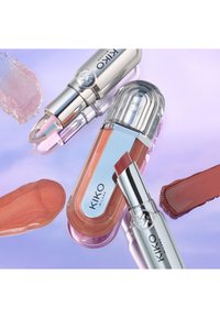 Trois produits de lèvres KIKO Milano : un rouge à lèvres en bâton argenté et transparent, un gloss rectangulaire rose clair avec des accents réfléchissants, et des échantillons de teintes.