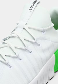 White athletic shoe with a textured upper, featuring white laces and hardware. Green accents on the heel and a flexible sole design.