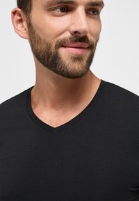 Zwarte v-hals t-shirt van soepel katoen, met een eenvoudig ontwerp en een nette halslijn, met zichtbare borsthaar en gezichtshaar.
