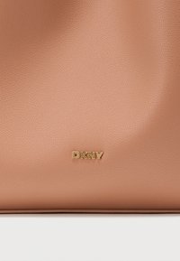 Τσάντα χειρός από δέρμα χρώματος ροδάκινου με υφή από κόκκους, με χρυσό λογότυπο "DKNY" μπροστά. Ομαλό, δομημένο σχήμα.