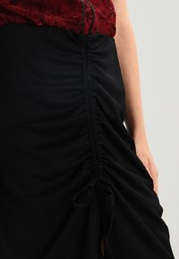 Černá midi sukně s nabíranými bočními švy a detailem na šňůrku. Tkanina je měkká a mírně pružná, s hladkou texturou.