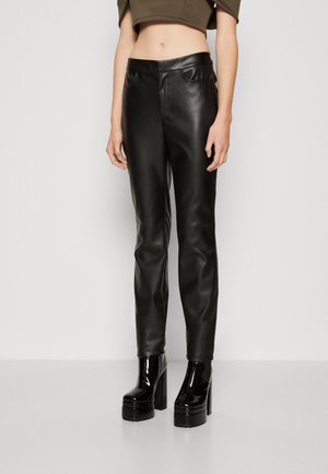 Pantalons noirs en cuir synthétique avec une coupe slim, présentant une taille avant et des poches, associés à des bottes à plateforme noires brillantes.