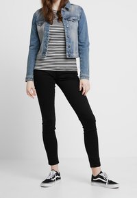 Jeansjacka med ljusblå tvätt, svart och vitrandig t-shirt, svarta tajta jeans och svarta sneakers med vita sulor.